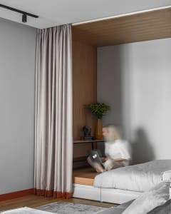 A minimalist bedroom with wooden furniture and a large window covered by curtains.