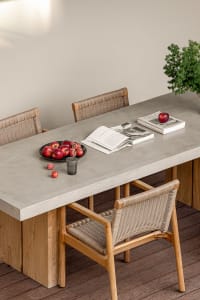 Modern dining room with concrete table, woven chairs, and plate of apples on the table.