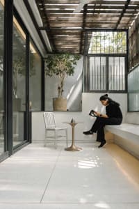 A minimalist living space with a concrete floor, a white chair, a small table with an object, and a potted plant.