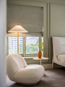 A modern bedroom featuring white upholstered furniture, a floor lamp, and a small round table with a vase containing greenery