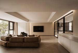 A modern minimalist living room with a concrete floor, brown leather sofa, and a large flat-screen TV mounted on the wall.