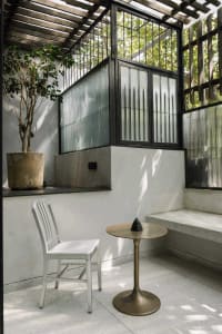 A modern industrial design space featuring a concrete floor, metal furniture, and natural light filtering through a pergola.