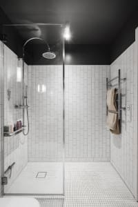 Modern bathroom with white tiled walls and floor, a glass shower enclosure, and minimalist design.