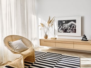Modern, minimalist living room featuring a wicker armchair with a white cushion, a wooden sideboard with a black and white fr