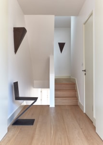A modern minimalist entryway featuring a wooden staircase with minimalist railings, white walls, and a black metal bench.