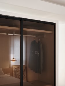 Minimalist closet with glass doors and wooden interiors, featuring casual attire hanging on a rail.