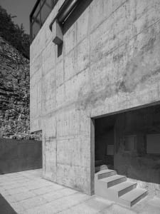 Modern concrete building facade with steps leading into a dark interior.