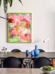 A vibrant abstract painting on a white wall above a dining room table with black chairs.