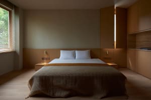 A modern minimalist bedroom featuring wooden walls and a bed with a white bedspread and a yellow blanket.