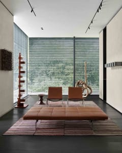 Modern minimalist living room with brown leather chairs, wooden side table, concrete floor, and large windows with blinds.