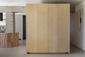A minimalist wardrobe cabinet made of light-colored wood, featuring four vertical panels.