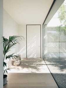 Modern minimalist entryway with wooden flooring, glass walls, and a light-filled courtyard.