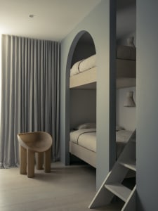 Modern minimalist bedroom featuring wood bunk beds with gray curtains and a unique brown tube-shaped chair.