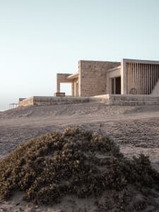 A minimalist vacant interior with stone walls and wooden structures against a clear sky.