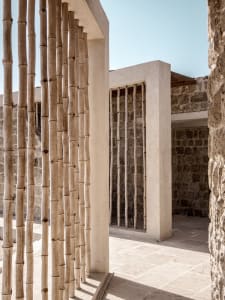 A modern architectural structure featuring tall wooden poles and stone walls.