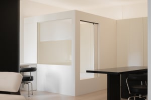 A modern office space with transparent glass partitions and white panel walls.