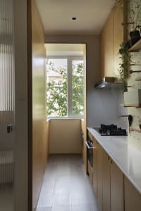 A minimalist kitchen with a white countertop and wooden cabinets, featuring a large window
