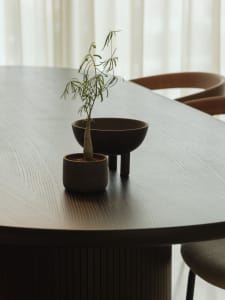 A modern table setting with a wooden table and a small plant in a decorative pot.