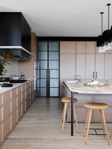 A modern kitchen featuring marble countertops and cabinets, with a central island and stools, in a residential setting.