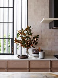 A modern kitchen with wooden cabinets and marble countertops featuring a potted plant and kitchen utensils.