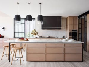 A modern residential kitchen featuring a large island with marble countertop and wooden drawers. The kitchen includes a backs