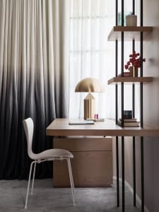 A modern workspace featuring a wooden desk with a brass lamp, and tall black and white curtains