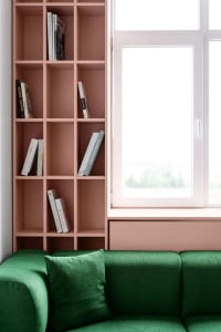 A modern living room featuring a green sofa with a bookshelf and a window.