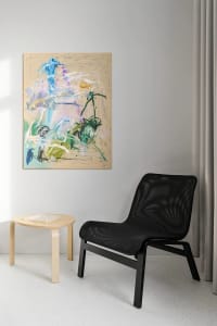 A modern black frame chair in a minimalist living room setting with an abstract painting on the wall and a round wooden side 