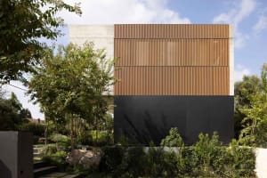 A modern house with a wooden facade and concrete lower sections surrounded by lush greenery.
