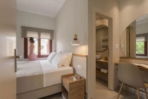 A minimalist bedroom with a white and neutral color theme, featuring a bed, nightstand, and bathroom access