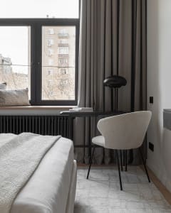 Minimalist bedroom featuring a white bed with textured fabric, a black desk, and a beige chair.
