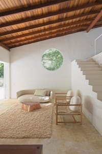 A minimalist living room with concrete and wooden elements, featuring a circular window.
