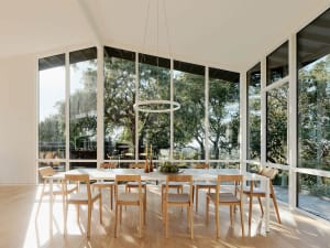A modern dining room featuring a large table surrounded by wooden chairs, with a hanging circular light fixture and large win
