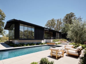 A modern minimalist house with large glass windows and a metal roof.
