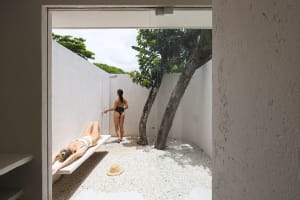 A modern outdoor shower with concrete walls and floors, featuring a shower head and a bench for relaxing under the sun.