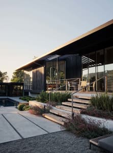 Modern residential exterior featuring wood, glass, and concrete materials with a terrace.