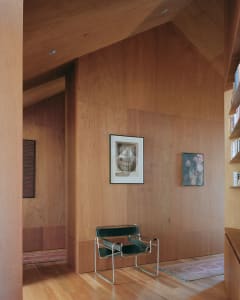A minimalist living room with wood paneling, featuring a modern chair and framed artwork.