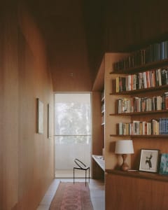 A cozy modern home library featuring tall shelves filled with books, a stylish chair, and a window providing natural light.