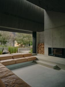 Modern industrial living room with concrete walls and floor, featuring a leather sofa and a concrete fireplace.