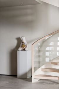 A modern staircase features glass railings and a wooden step, accompanied by a decorative glass sculpture of a bear holding a