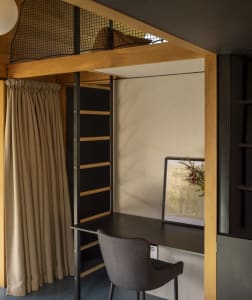 A minimalist home office featuring a black desk, grey chair, wooden shelves, and a framed piece of art.