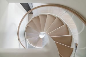 A modern wall-mounted wooden staircase with a white railing, viewed from above.