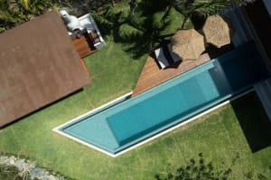 A modern backyard featuring a concrete pool with water, surrounded by a well-maintained lawn and shaded seating areas.
