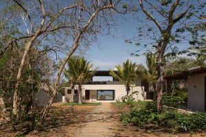 Modern exterior of a concrete home with a clear blue sky and surrounded by trees.