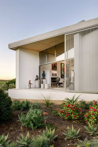 Modern house exterior featuring a concrete structure with large sliding doors and a landscaped garden.