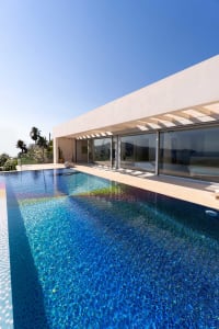 A modern house featuring a glass wrap-around pool under a clear blue sky.