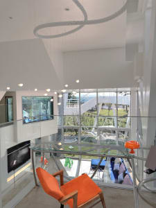 A modern living room with large glass windows, a glass table, and sleek metal accents.