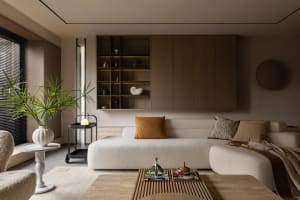 A modern living room with a minimalist design, featuring neutral-toned furniture, a large window, a coffee table with magazin