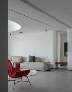 A minimalist living room featuring white walls, a modern sofa, and a single red accent chair.