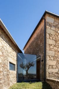 A modern stone house with large glass window and rustic exterior.